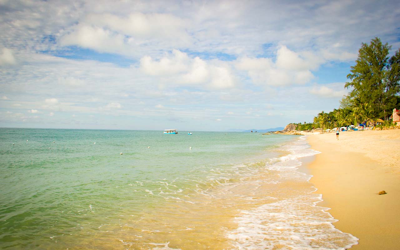 A tranquil beach in Thailand with golden sand, clear waters, and a partly cloudy sky.